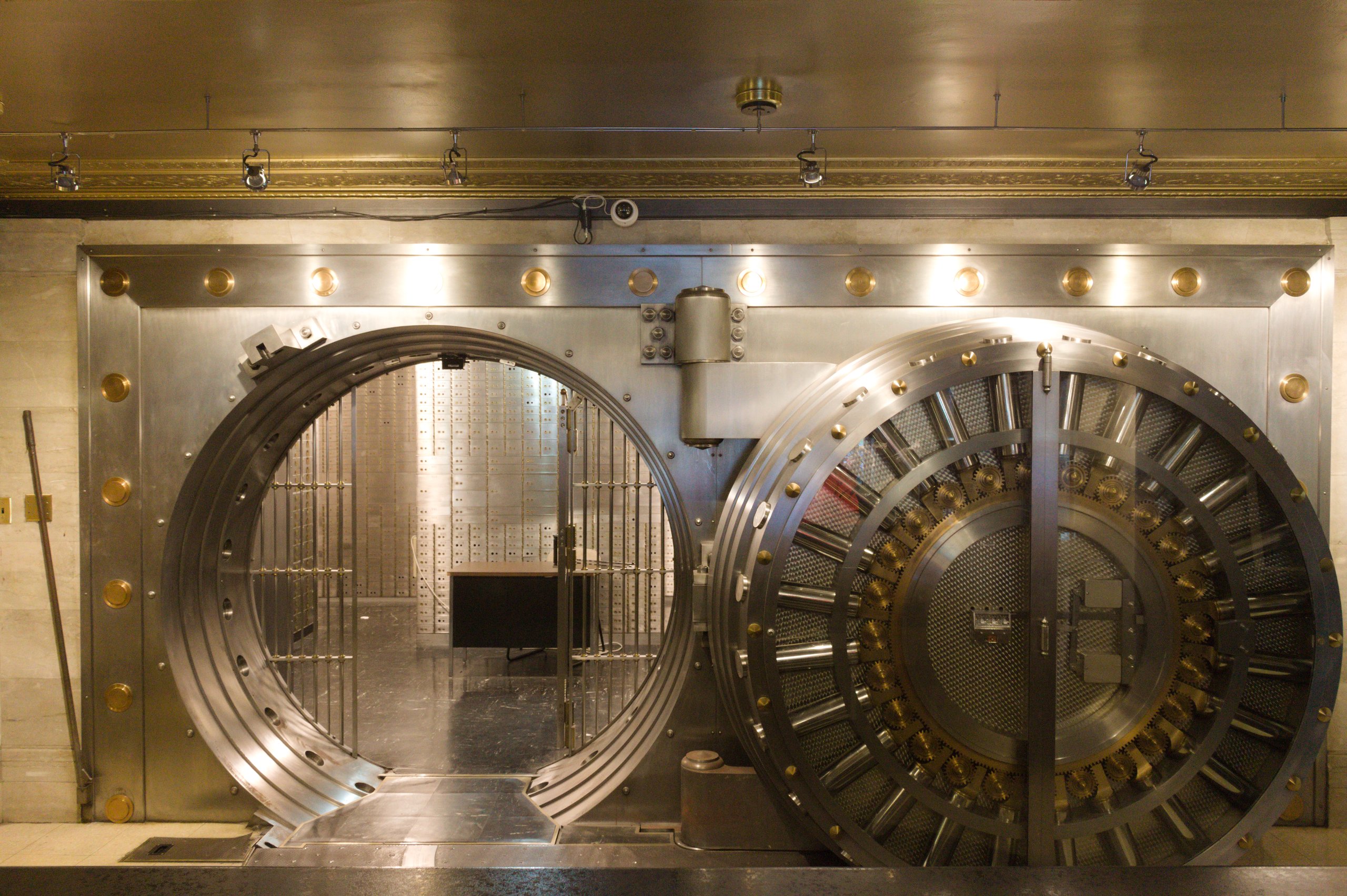 A massive round steel bank vault door standing open, showing its locking bolts