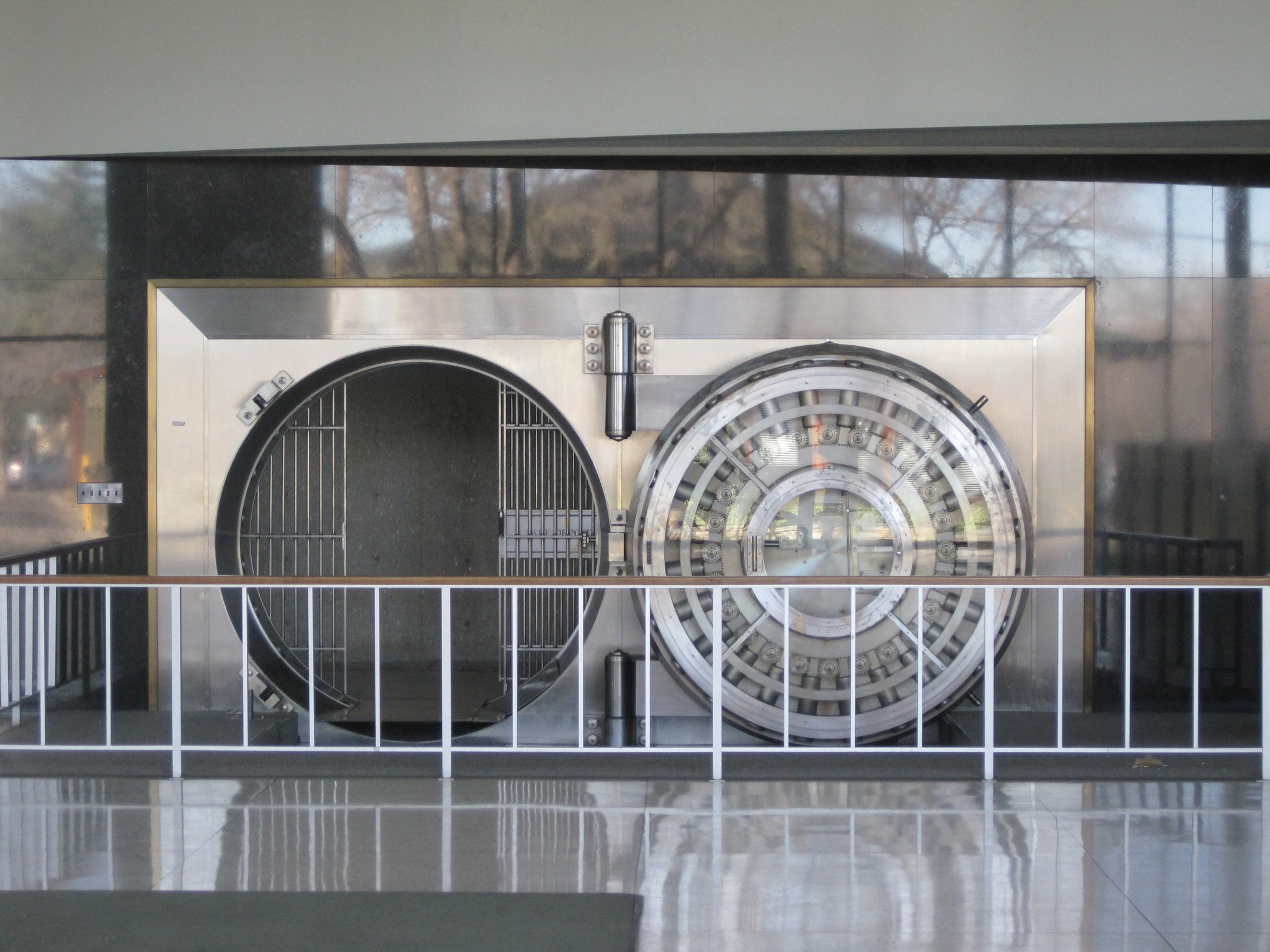 A large round steel bank vault door standing open behind a railing