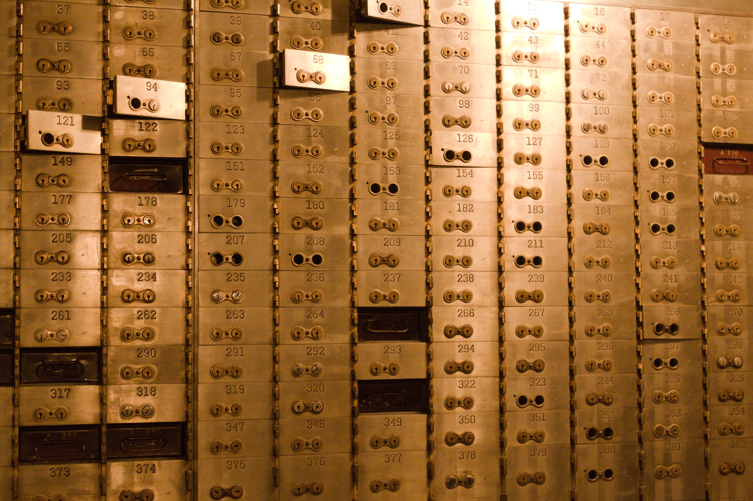A wall of numbered brass safe deposit boxes in a bank vault
