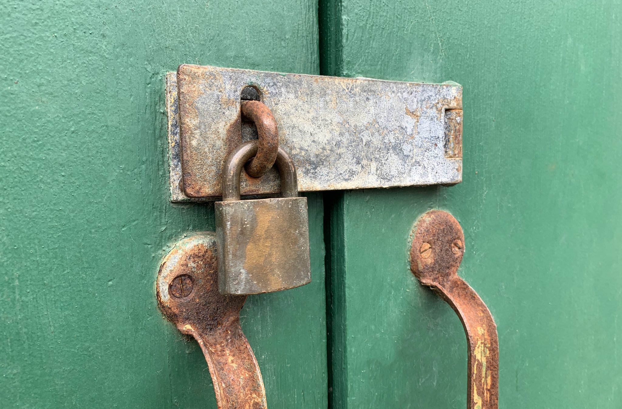 A rusty padlock securing a hasp on a green wooden door