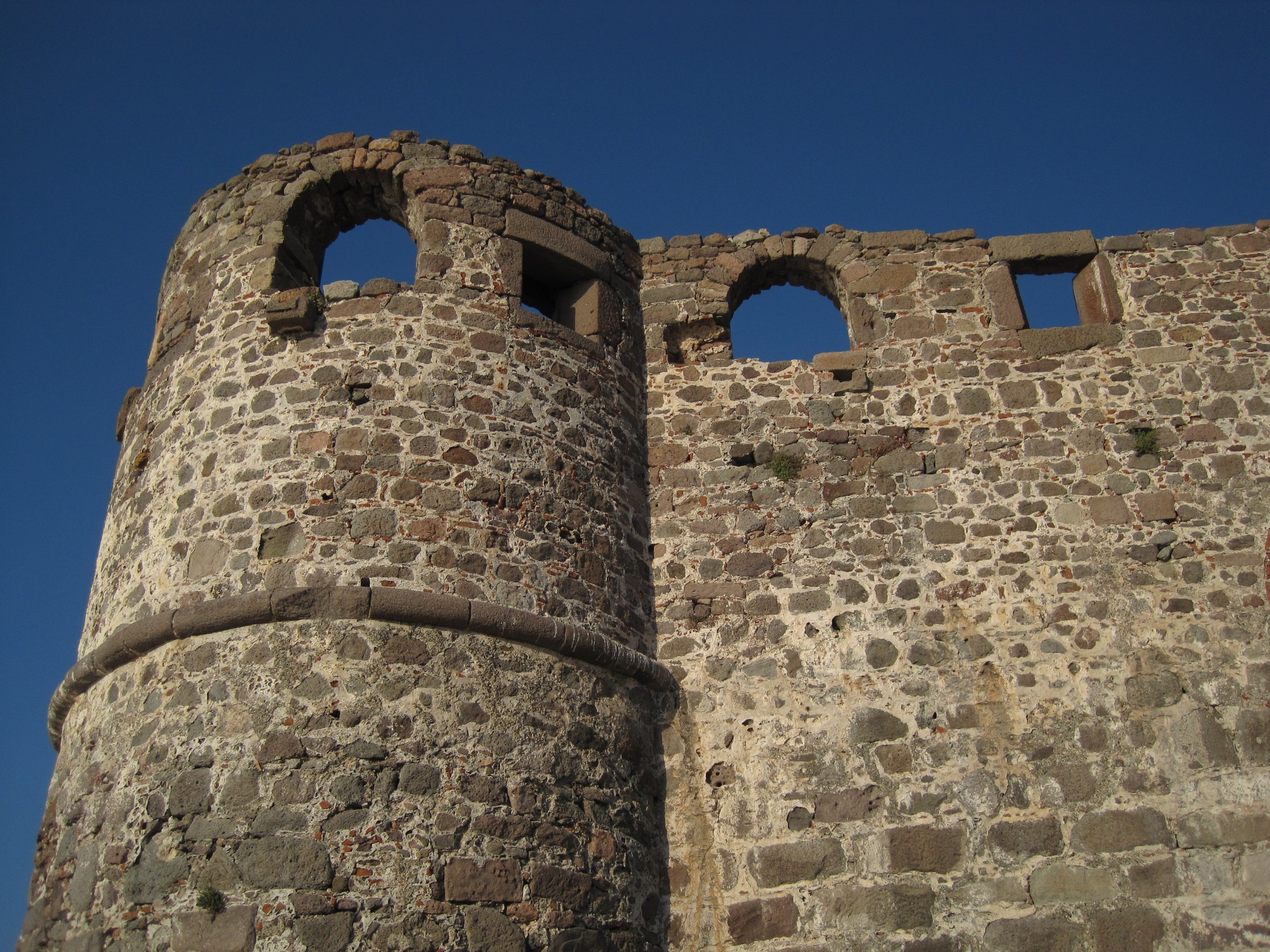 A round medieval stone castle tower and wall against a clear blue sky